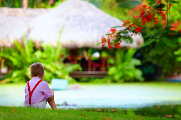 cute kid sitting on green lawn near the tropical lake