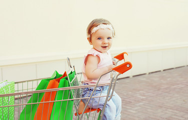 Happy smiling baby sitting in trolley cart with colorful shoppin