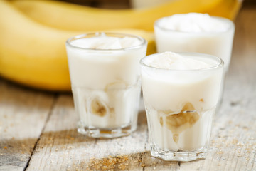 Fresh homemade banana yogurt in glass on old wooden table, selec
