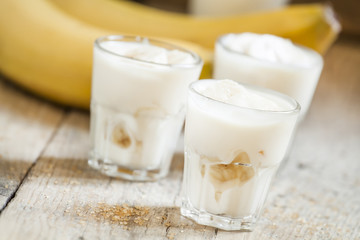 Fresh homemade banana yogurt in glass on old wooden table, selec