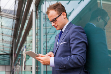 Caucasian businessman outside office using white tablet pc in front of office block.