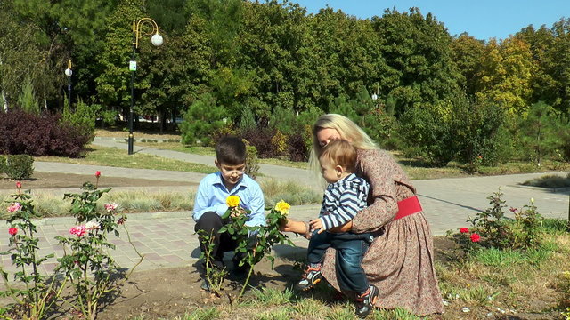 Mom kid shows a yellow rose in a city park