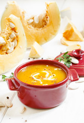 Pumpkin soup in a red bowl on white wooden background, selective