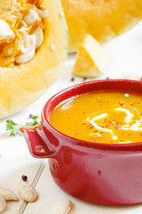 Pumpkin soup in a red bowl on white wooden background, selective