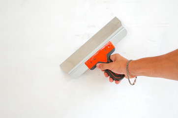 Hand holds trowel at an angle to the plastered wall, completing