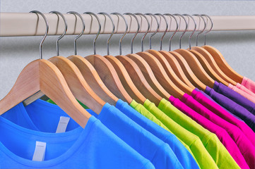 Multicolored women's t-shirts hang on wooden hangers.