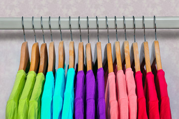 Multicolored women's t-shirts hanging on wooden hangers.