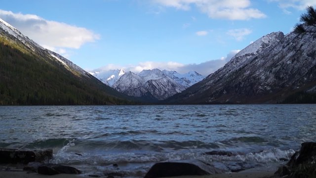 Middle multinskoe lake in autumn Altai. Surf on the stone beach and views of the snowy peaks of the Altai Mountains.