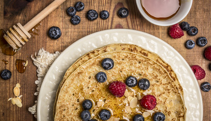 delicious pancakes with fresh berries with honey, almonds cup of tea with honey spoon on white plate with napkin on wooden rustic background