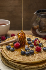 pancakes with fresh berries and honey spoon on wooden background close up