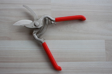 Pruning shears with two red handles and metal spring on beige floor.