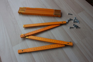 Two wooden meters and some nails on beige floor. One of the meter is folded and the other is unfolded.