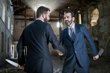 Dos hombres de negocios parecen hacer tratos mientrras esconden cuchillos