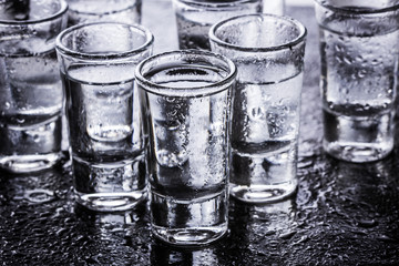 Vodka shot glass on wet black surface.