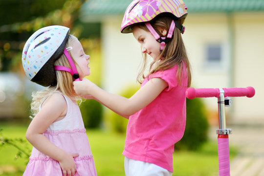 Little girl helping her sister to put a helmet on