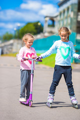 Two little girls roller skating and riding a scooter in the park