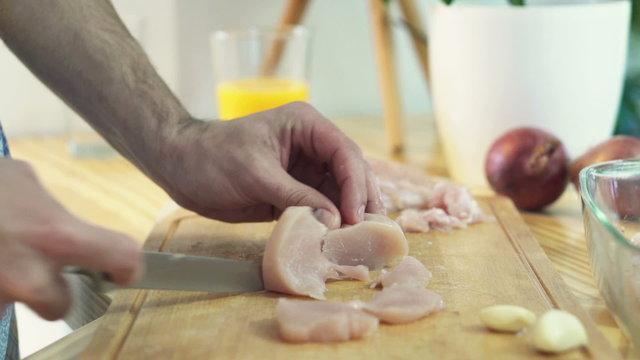 Man slicing chicken breast on chopping board in kitchen

