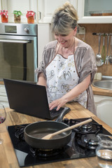 Smiling woman typing on laptop in the kitchen.
