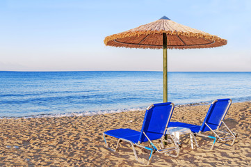 Two blue sunbed, straw umbrella on beautiful beach background