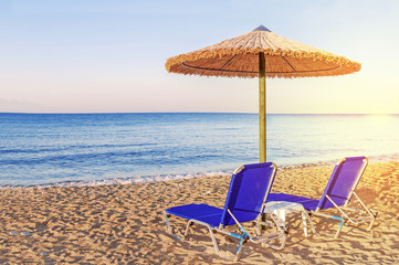Two blue sunbed, straw umbrella on beautiful beach background
