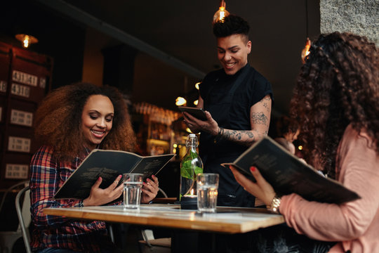 Young girls at cafe giving order to the waiter