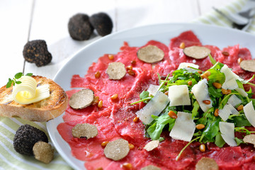 Feines Carpaccio vom Rinderfilet mit schwarzen Herbsttrüffeln und gerösteten Pinienkernen sowie Rucola mit geholbeltem  Parmesan