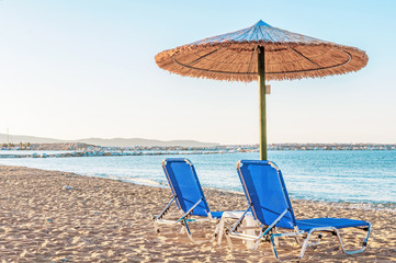 Two blue sunbed, straw umbrella on beautiful beach background