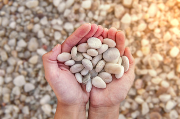 Woman hands holding small stones in hands on beach background with burning sun