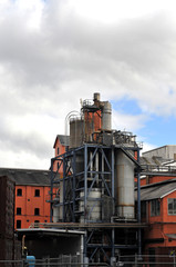 Red factory buildings and metal industrial devices of a sugar refinery with a cloudy sky background.