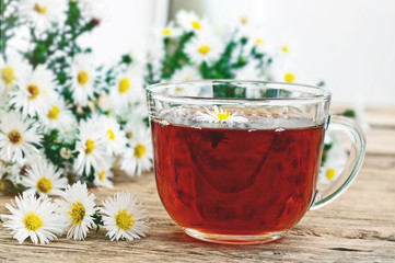 Black tea in a glass cup and chamomile flowers