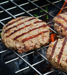 Burgers patties cooking over flames on a grill.