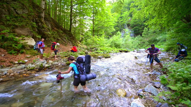Mountaineers crossing the river barefoot in a summer day