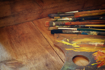 top view of set of used paint brushes and palette over wooden table
