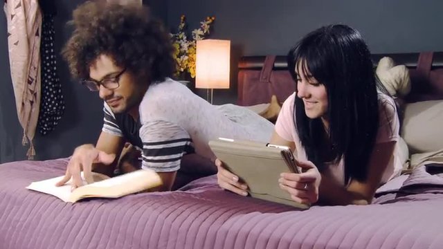 Couple at home at night in bed reading book and ebook