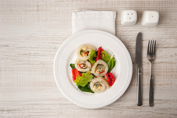 Squid roll with cheese and vegetables on the ceramic plate  with cutlery top view