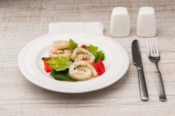 Squid roll with cheese and vegetables on the ceramic plate  with cutlery
