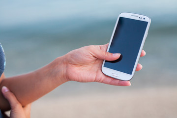 Pretty girl standing on the beach near the sea with smarphone.
