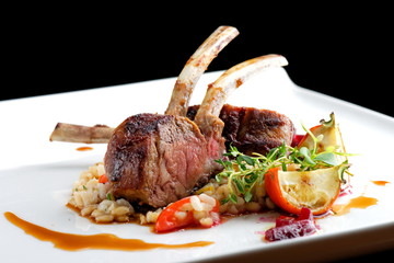 Fine dining roasted Lamb Chops on whole grain rice, mini aubergines and a sauce garnished with beerot, tomato and basil