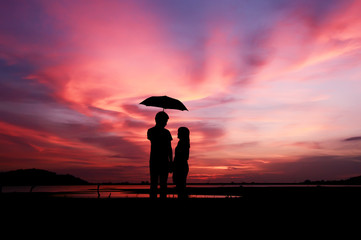 Silhouette of romantic couple holding umbrella with sunset sky © maybeiii