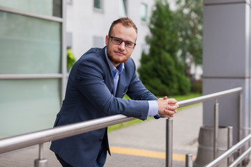 Portrait of young businessman with beard standing in front of office bulding.