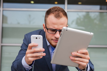 Caucasian businessman outside office using mobile phone and tablet pc.