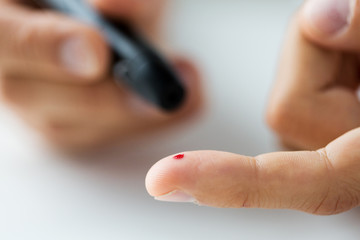 close up of male finger with blood and glucometer