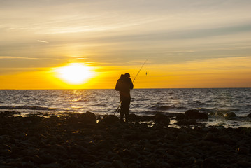 Angler fishing at the coast in an Autumn sunset