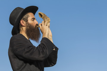 Orthodox Jewish man blast in Shofar at Rosh Hashana holiday on blue sky background