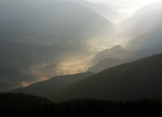 Mountain valley village in the fog and sun rays of dawn