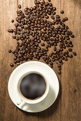 White coffee cup and coffee beans on wood background.