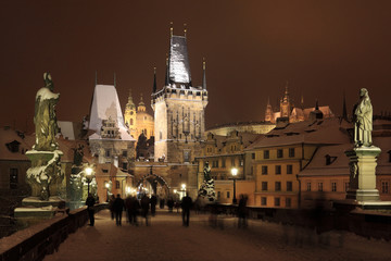 Fototapeta na wymiar Night colorful snowy Prague gothic Castle with Bridge Tower and St. Nicholas' Cathedral and Sculptures from the Charles Bridge, Czech republic