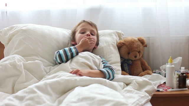 Sick child boy lying in bed with a fever,resting, coughing and blowing his nose