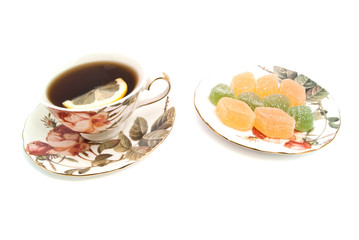 cup of tea with lemon and fruit candies on white