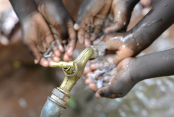 Hands of African Children Cupped under Tap Drinking Water Malnutrition. Hands of African black boys and girls with water pouring from a tap. It affects people and especially children in Africa.